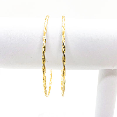 pair of 14k Gold Filled Single Twist Bangle by Judie Raiford handing on white bracelet display stand