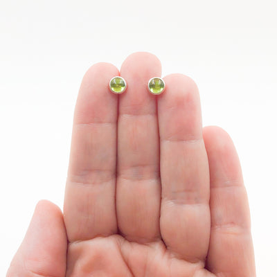 6mm Peridot Cabochon Stud Earrings by Judie Raiford held in hand