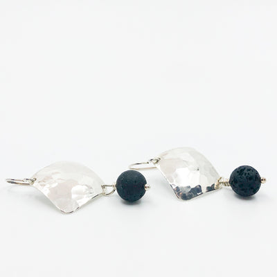 side angle flat lay of Sterling Ball Pein Hammered Goat Earrings with black lava by Judie Raiford