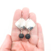 Sterling Ball Pein Hammered Goat Earrings with black lava by Judie Raiford held in hand