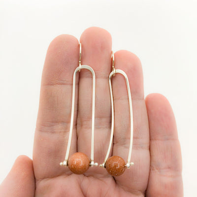 Long Brewish Earrings with Goldstone by Judie Raiford held in hand