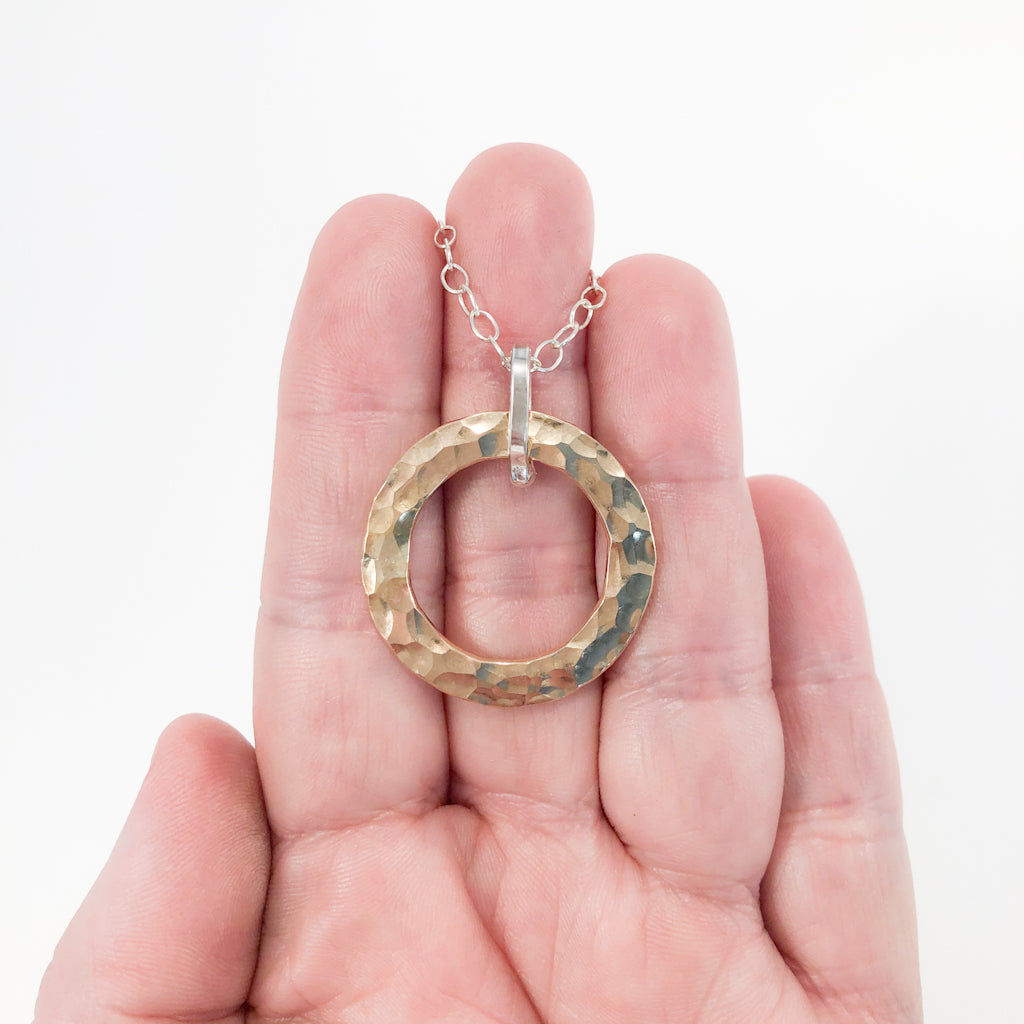 Sterling and 14k Gold Filled Ball Pein Hammered Circle Pendant Necklace by Judie Raiford held in hand