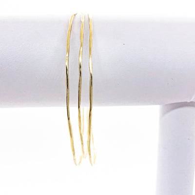 14k Gold Filled Skinny 3-Piece Bangle Set by Judie Raiford hanging on white bracelet display stand