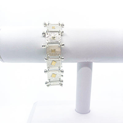 Sterling and 22k Singer Bracelet by Judie Raiford hanging on white bracelet display stand