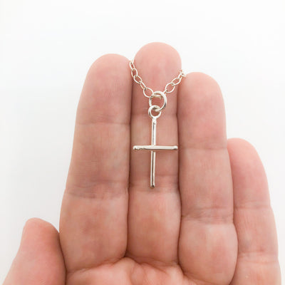 Sterling Tiny Cross Necklace by Judie Raiford held in hand