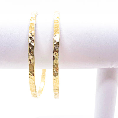 pair of 14k Gold Filled Ball Pein Hammered Bangles by Judie Raiford hanging on white bracelet display stand