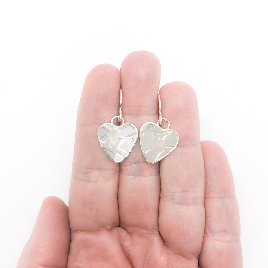 flat lay view of Sterling Silver Small Hammered Heart Earrings by Judie Raiford held in hand
