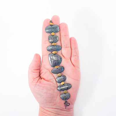 held in hand view of Pebble Bracelet in Oxidized Sterling and 22k Gold by Donna Burdic
